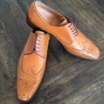 Brown leather brogue shoes on wooden floor.